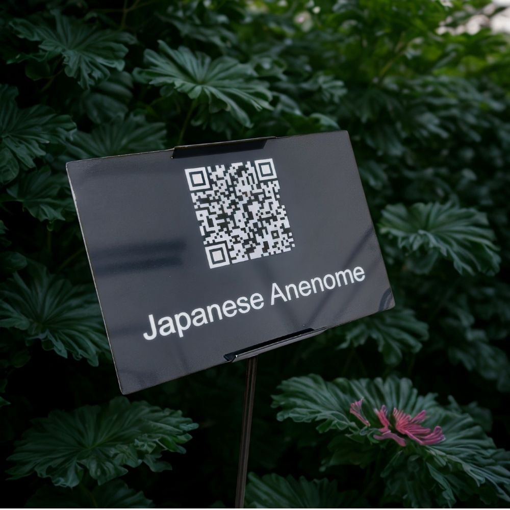 Black metal QR code label mounted in a holder at a botanical garden exhibit